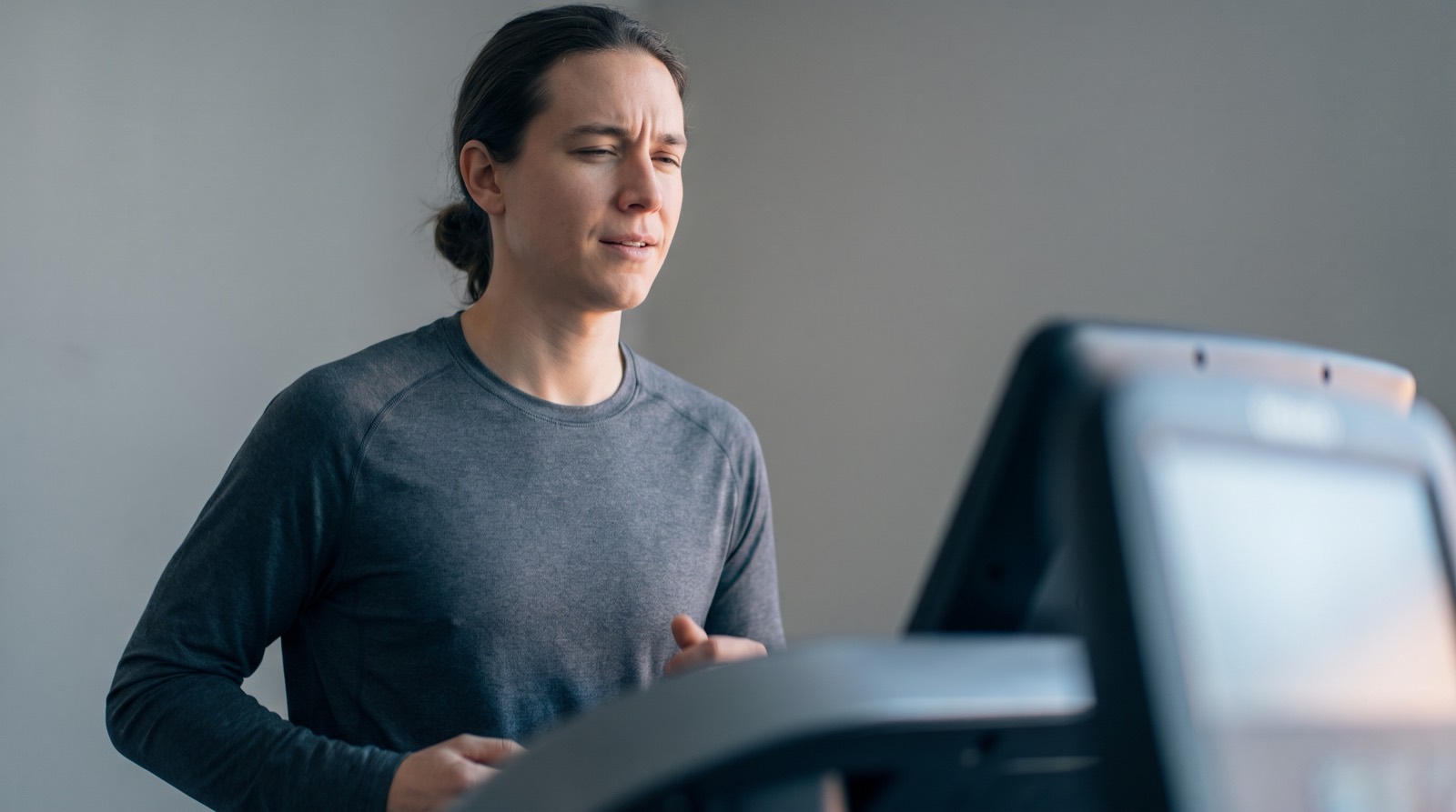 A runner on a treadmill turning to look at the display with a slightly uncertain expression, the screen a soft blur, lit by cool overcast daylight
