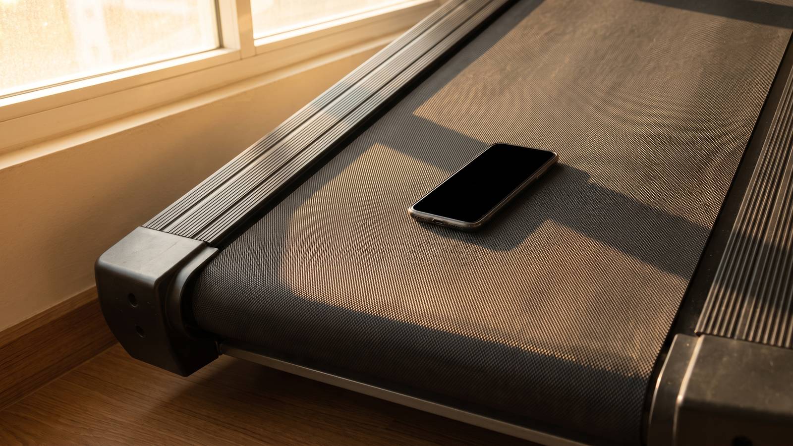 An iPhone lying flat on a stopped treadmill belt in warm evening light, ready to read the slope of the deck with the Level