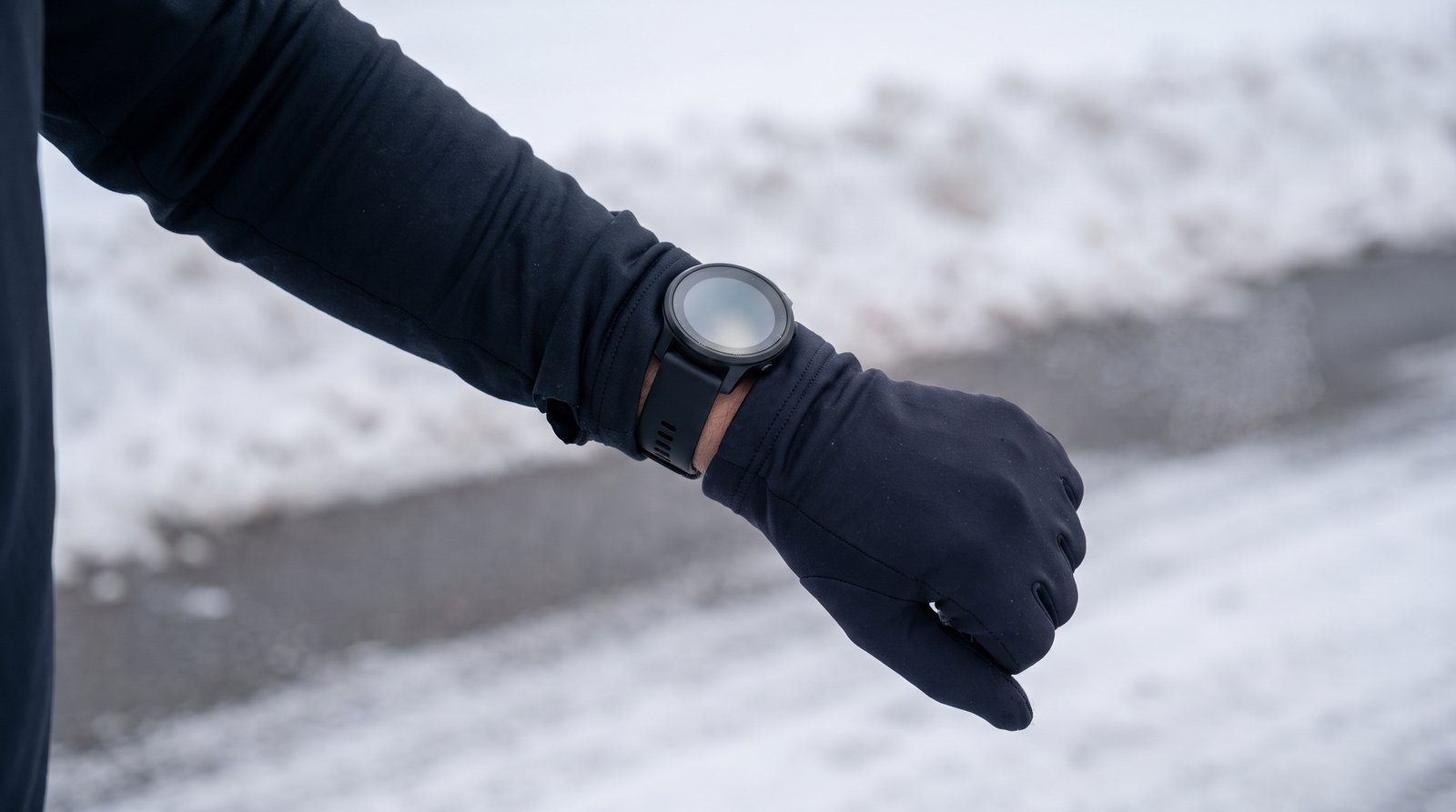 A runner's gloved wrist and sport watch on a snowy road at midday, flat gray winter light