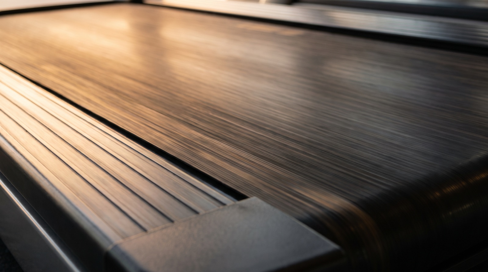 A close view of an empty treadmill belt moving fast, its surface blurred along its length in warm golden-hour light