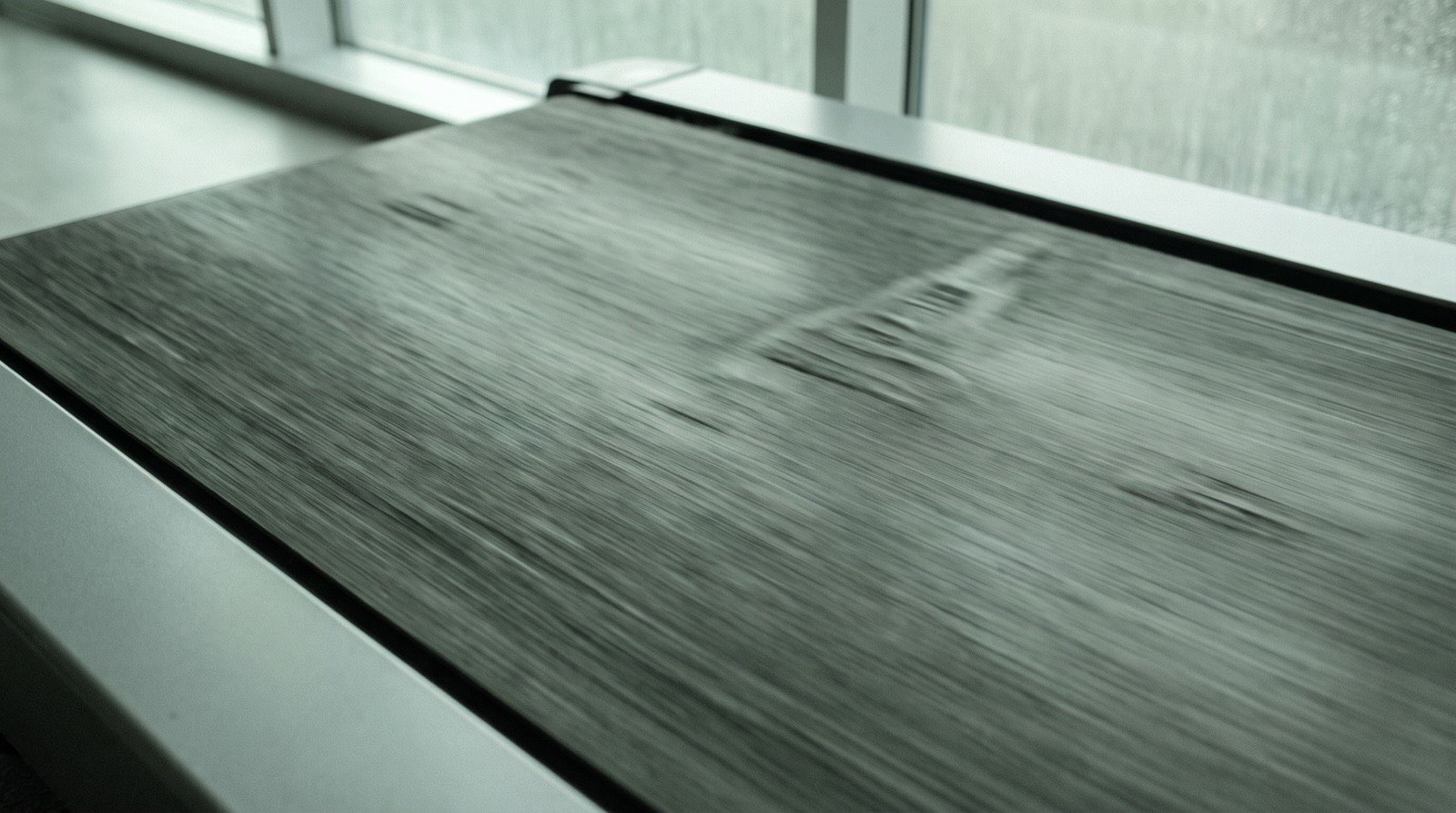 A close view of a treadmill belt running at speed, its tread ridges smeared into directional blur, in soft even overcast daylight